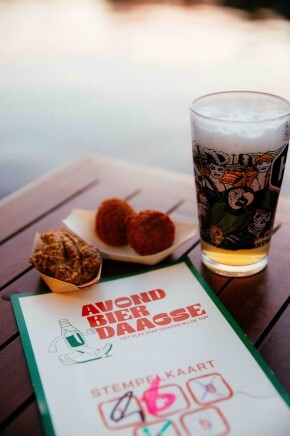 Een glas bier, snacks en een stempelkaart op een houten tafel bij zonsondergang.