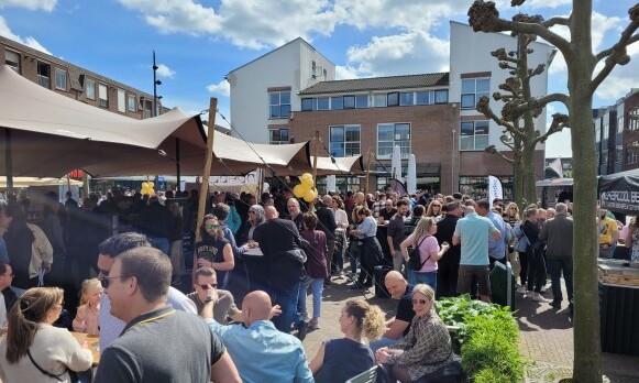 Mensenmassa op de Beuningse Bierproeverij onder tenten met gebouwen op de achtergrond.