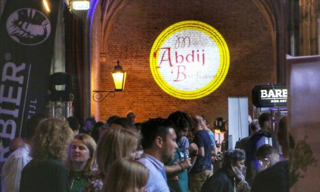 Drukbezocht Abdij Bierfestival met mensen, bierstands en een grote projectie op de muur.