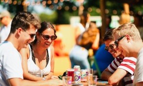 Vier jonge mensen lachen en praten aan een houten tafel tijdens het TAPT Festival.