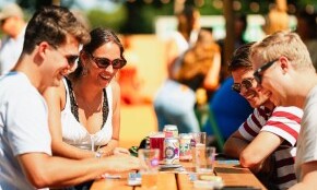 Vier personen spelen een bordspel aan een houten tafel op een festival.