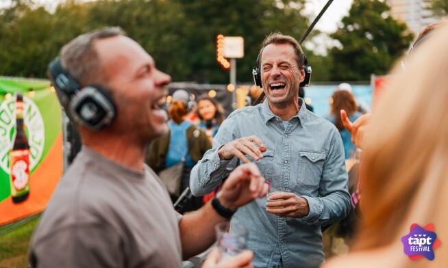 Mensen lachen en dragen koptelefoons op het TAPT Festival in een feestelijke sfeer.