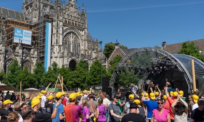 Mensen bij een buitenpodium voor een kathedraal tijdens een zonnig festival