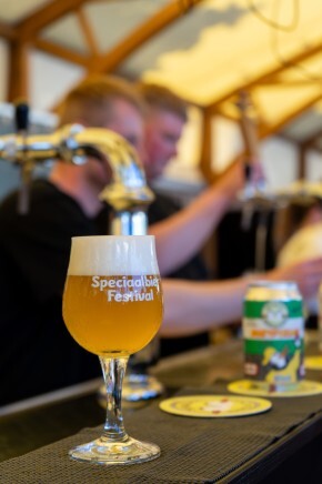 Glas speciaalbier op toog met festivalachtergrond.