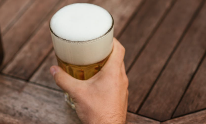 Hand houdt glas bier vast op een houten tafel