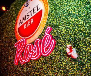 Amstel Rosé logo en glas van het bier door een heggetje