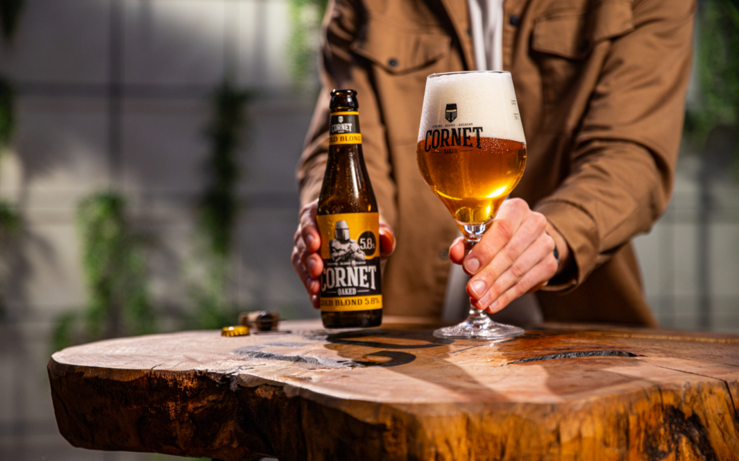 Cornet Gold Blond bier flesje en glas in de handen op een eikenhouten tafel