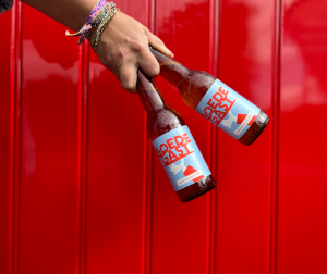 Goede Gast biertjes vastgehouden voor een rode achtergrond