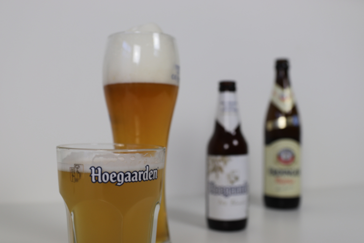 Witbier van Hoegaarden en Weizen van Erdinger in glazen met flesjes op de achtergrond