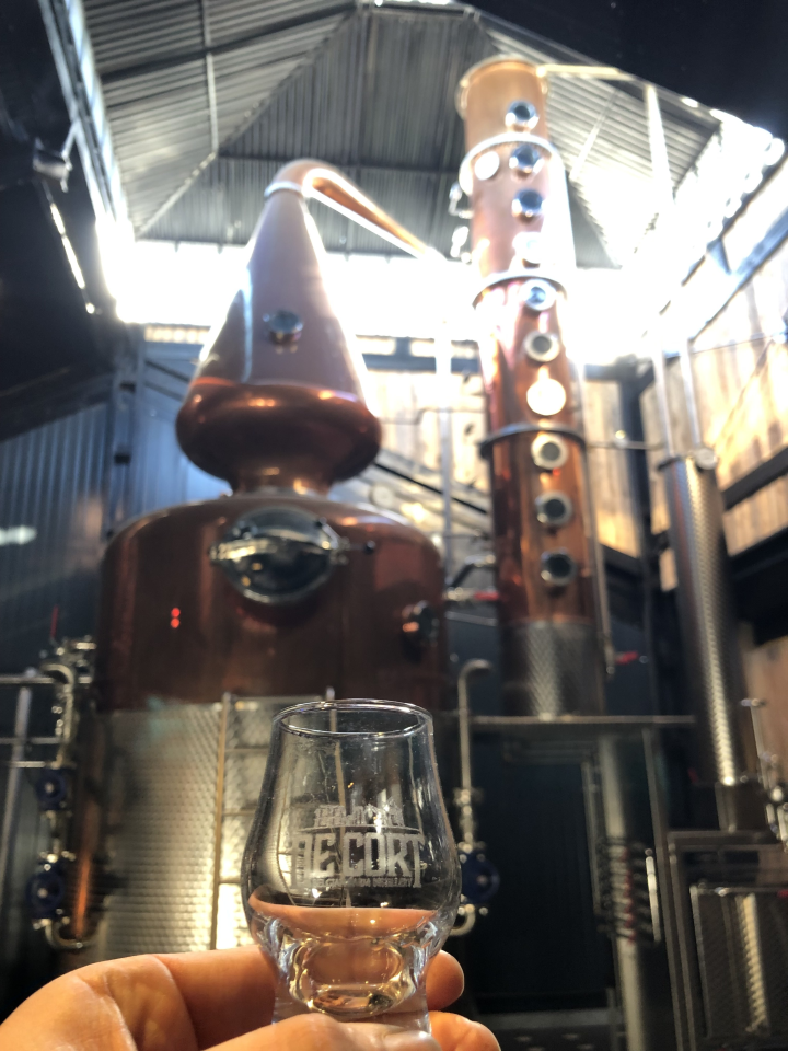 Proefglaasje bij De Cort Distillery met de distilleerketel op de achtergrond