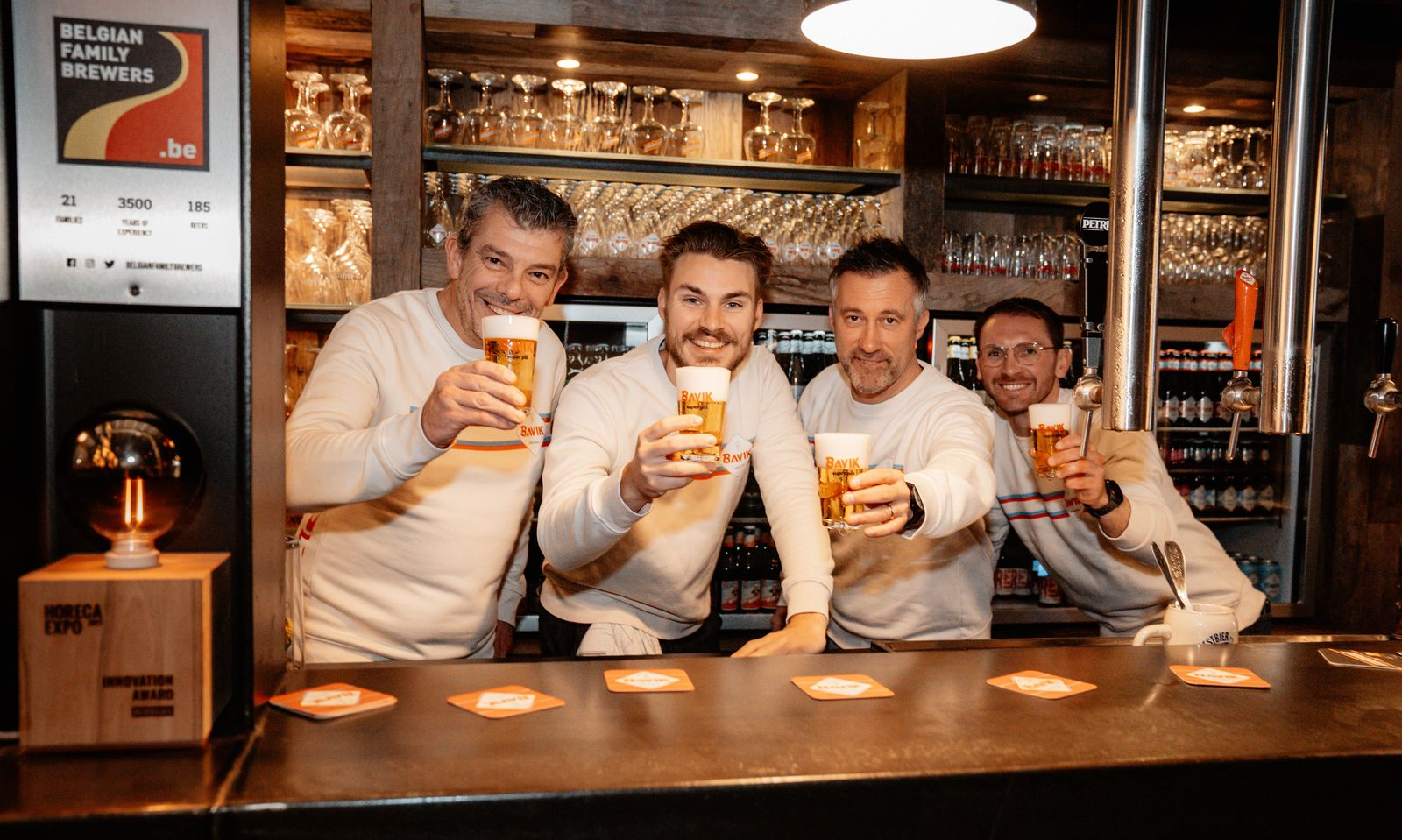 Vier mannen in een bar die glimlachend glazen bier omhoog houden.