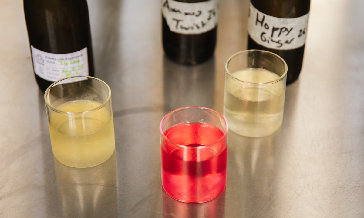 Drie glazen drankjes in verschillende kleuren voor donkere flessen op een tafel.