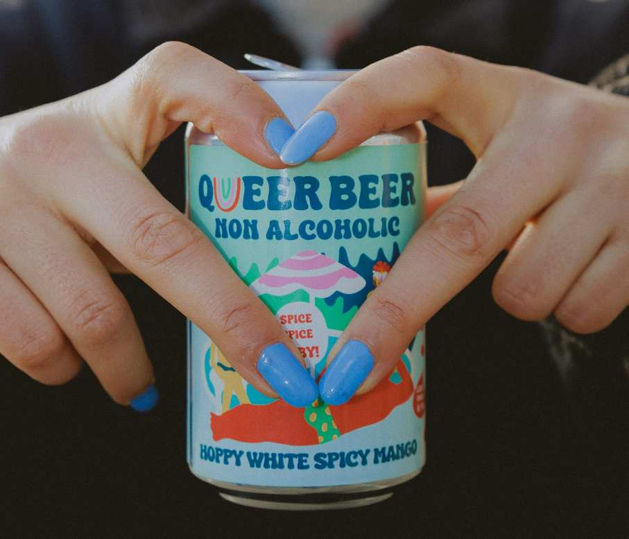 Handen met blauwgelakte nagels houden een Queer Beer blik vast met kleurrijk etiket.