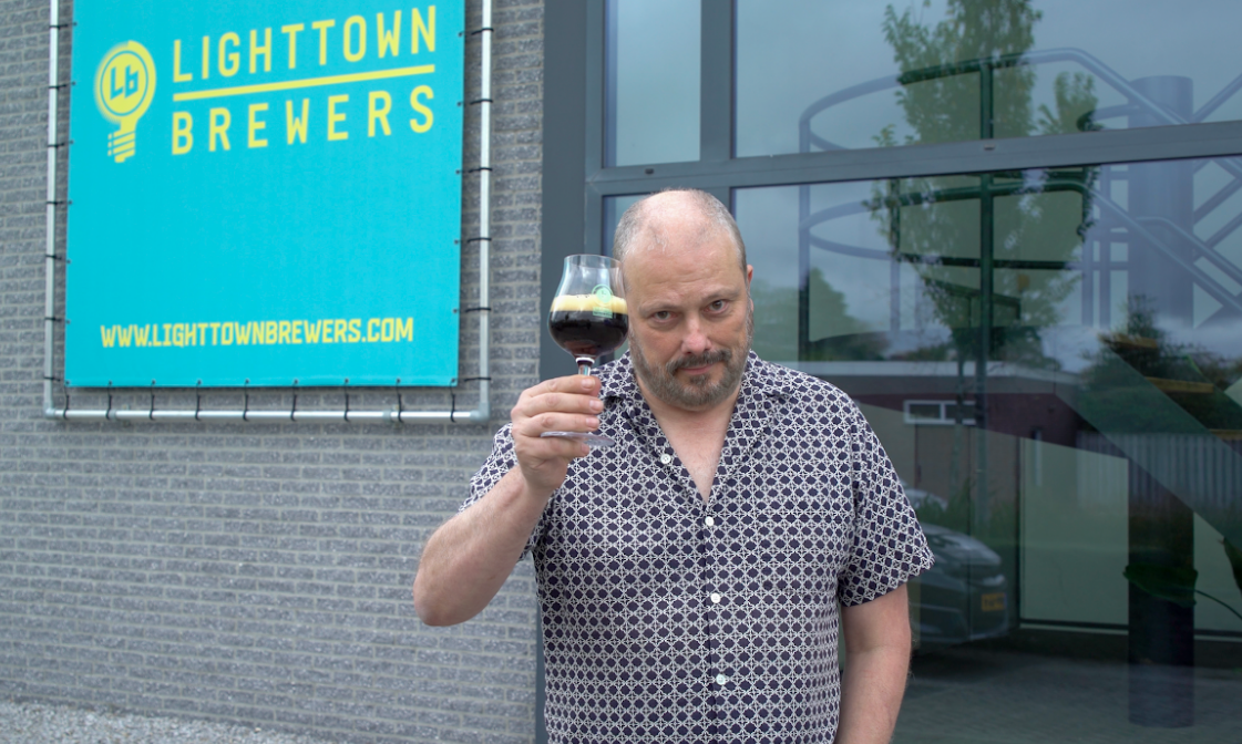 Erwin van Moll heft een glas donker bier buiten bij de Lighttown Brewers brouwerij.