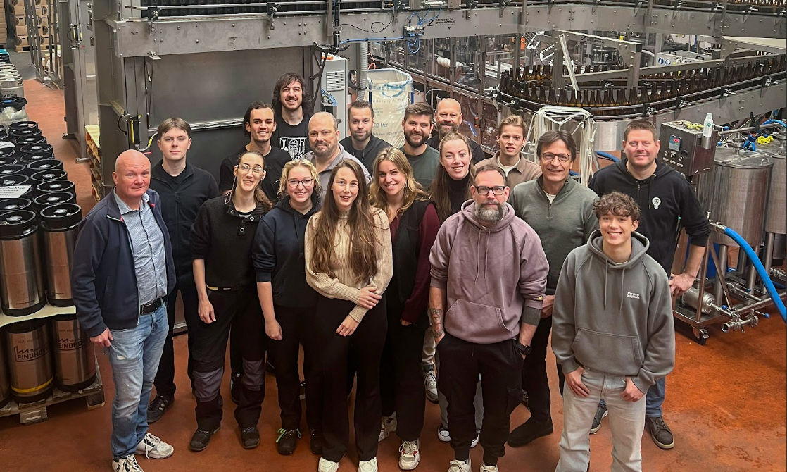 Groepsfoto van medewerkers Lighttown  Brewers in de brouwerij met brouwinstallaties en fusten op de achtergrond.