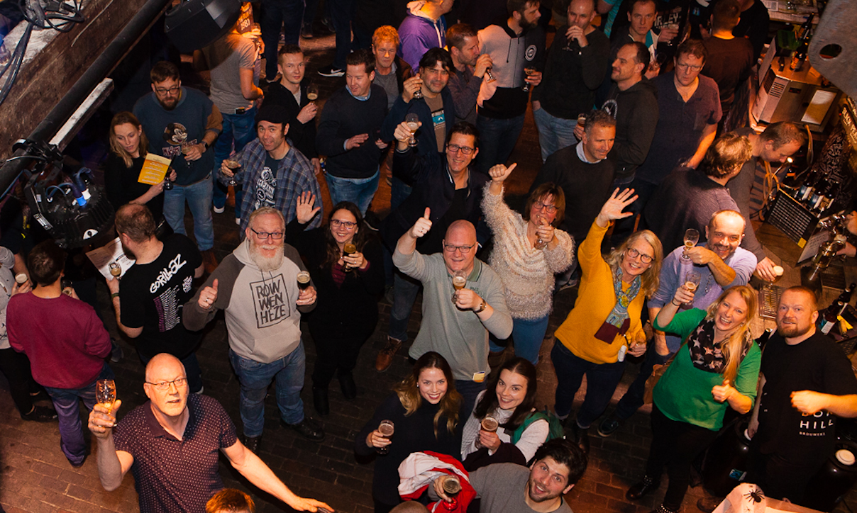 Mensen vieren samen in een druk café, kijkend naar boven met glazen in hun handen.