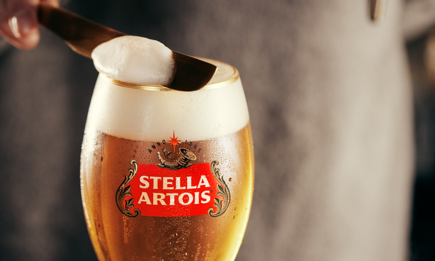 Close-up van een Stella Artois glas waarbij het schuim met een afschuimer wordt gladgestreken.