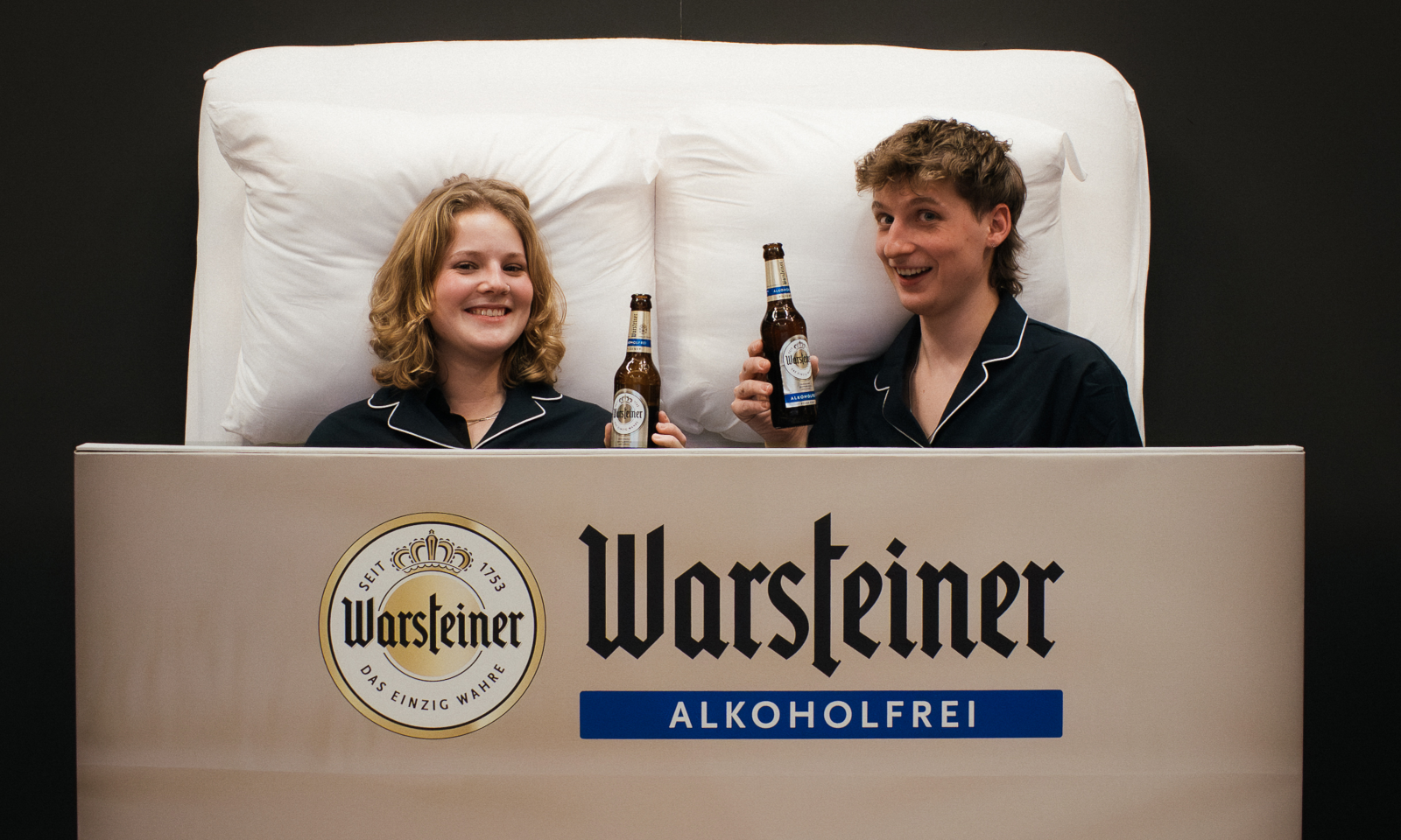 Twee personen in bed met Warsteiner flessen voor Dry January campagne.