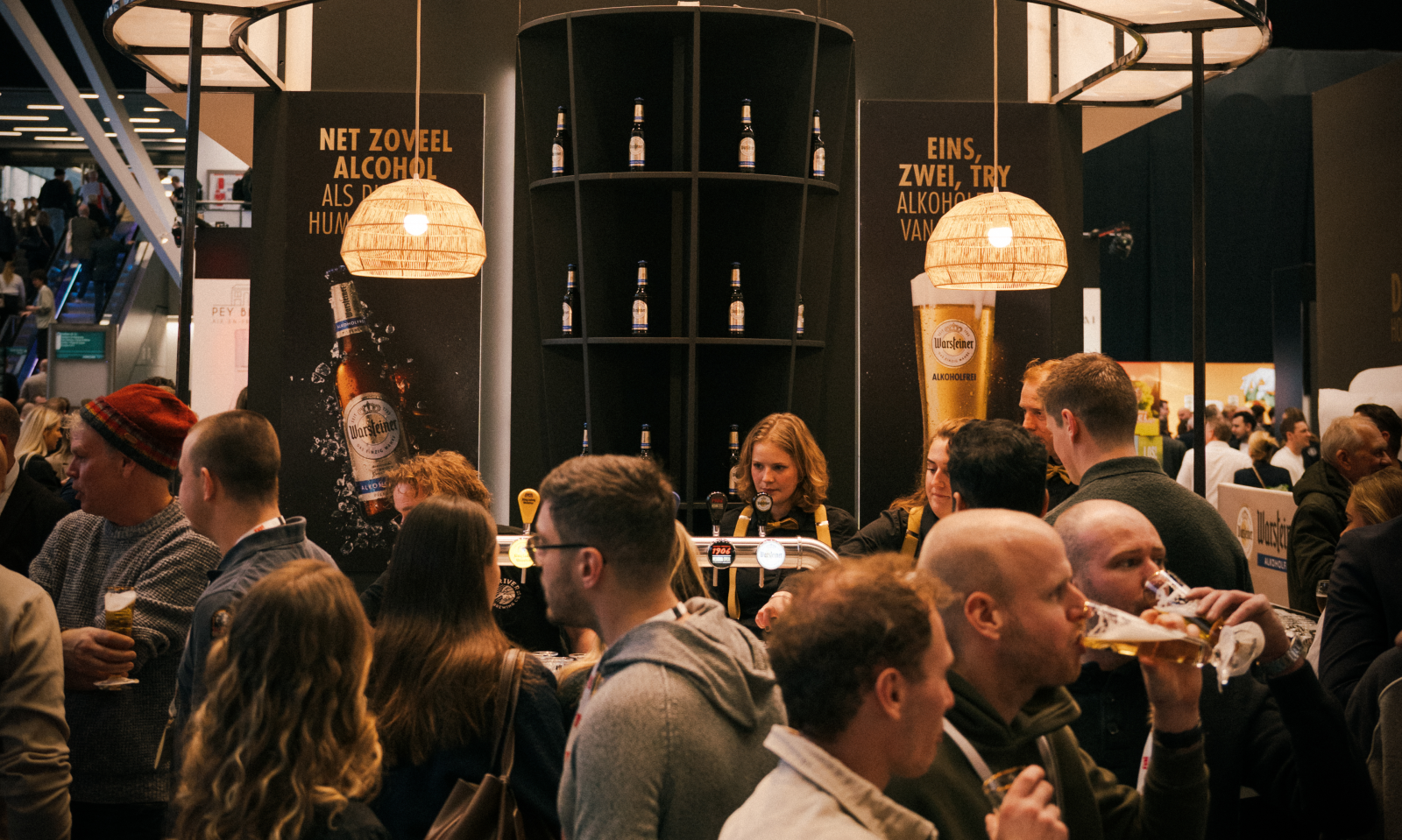 Mensen staan bij een stand van Warsteiner op een beurs, met reclames voor alcoholvrij bier.