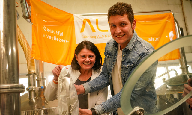 Twee personen werken samen in een brouwerij met ALS Stichting spandoek op de achtergrond.