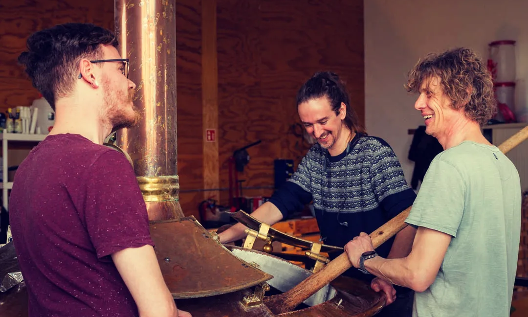 Drie mannen om een koperen brouwketel heen