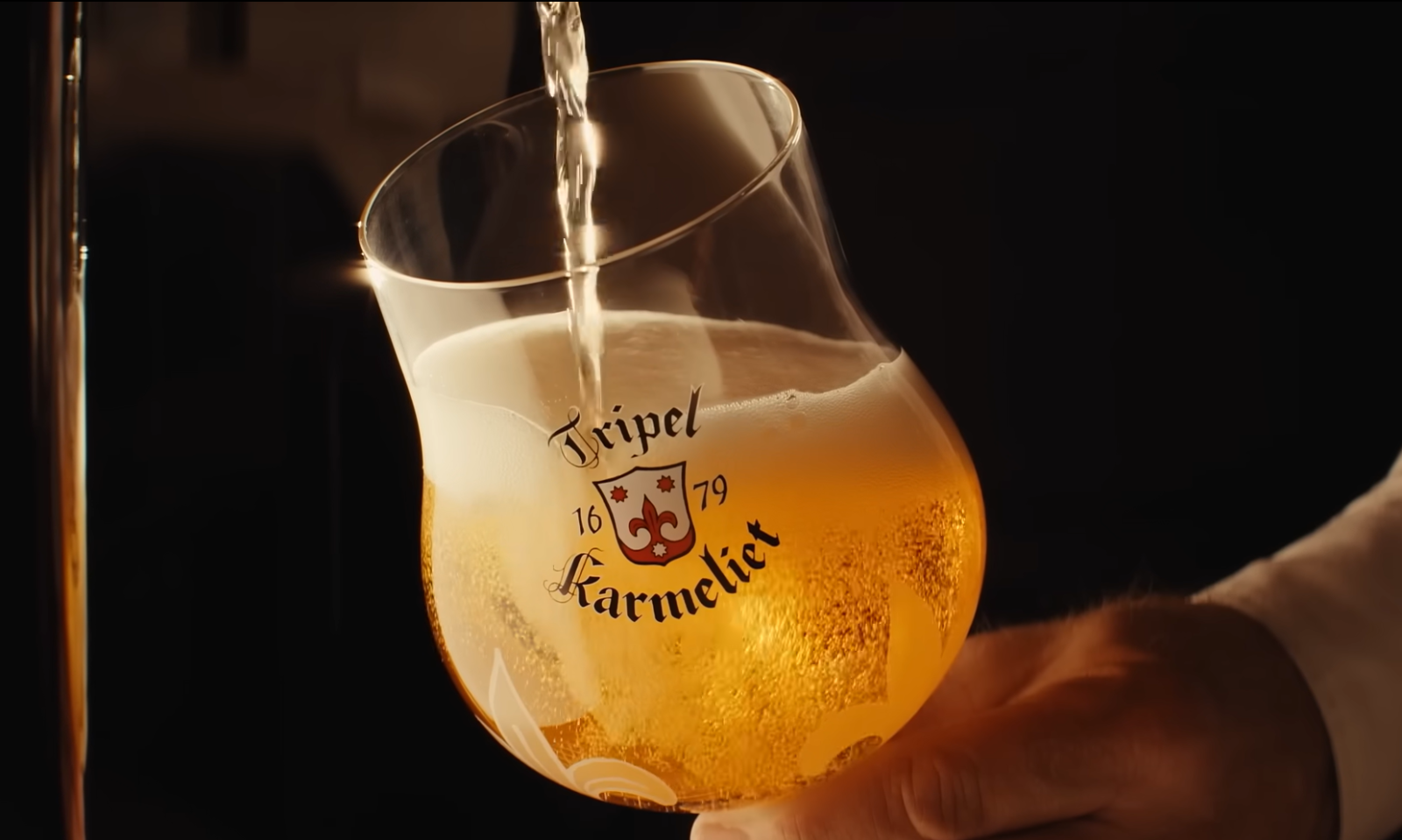 Een glas Tripel Karmeliet bier wordt geschonken met een rijke schuimkraag.