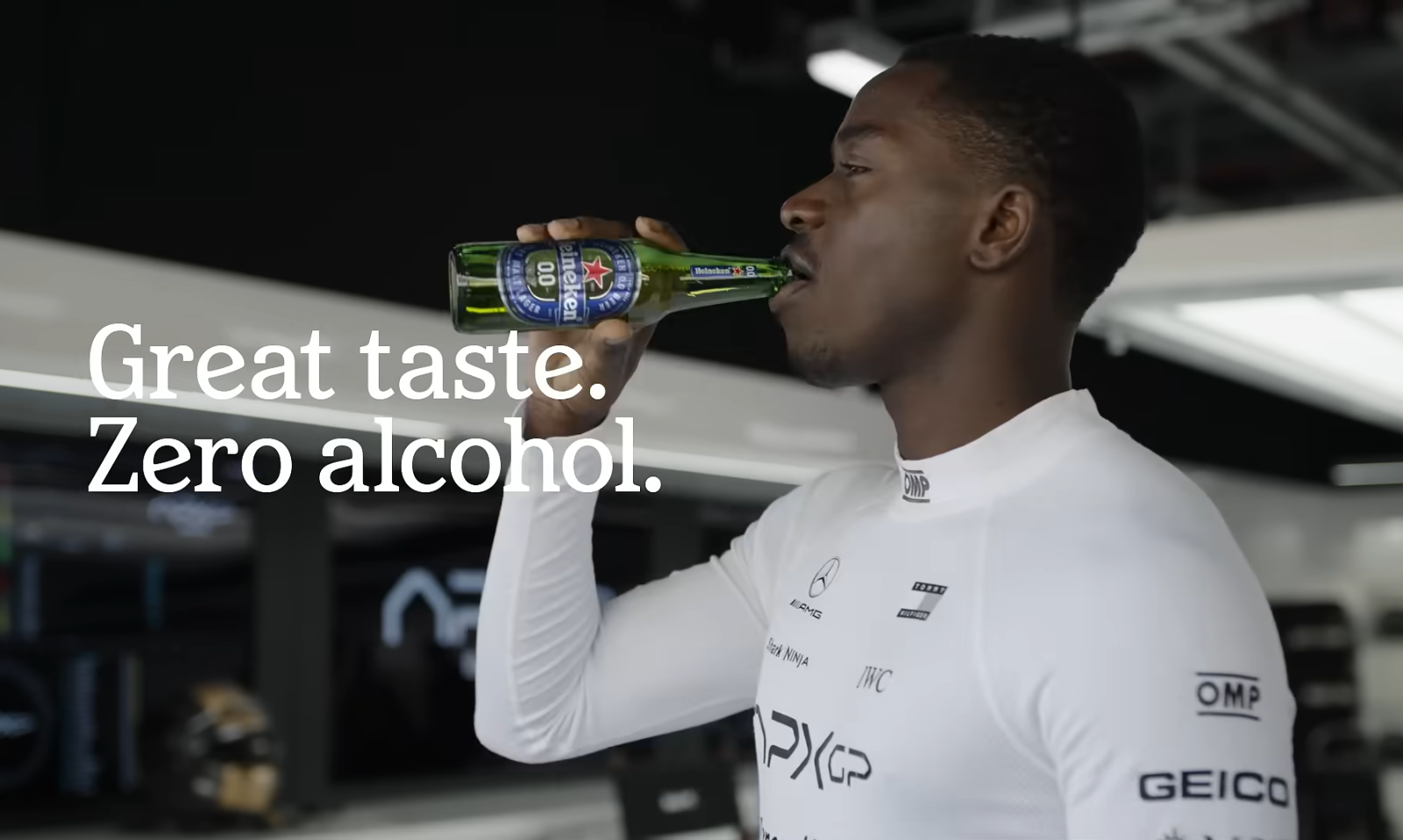 Man drinkt een fles Heineken 0.0 in een raceteam omgeving, tekst: 