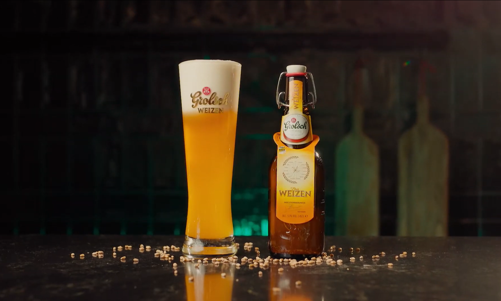 Een glas en een fles Grolsch Puur Weizen op een donkere ondergrond met gerstekorrels.