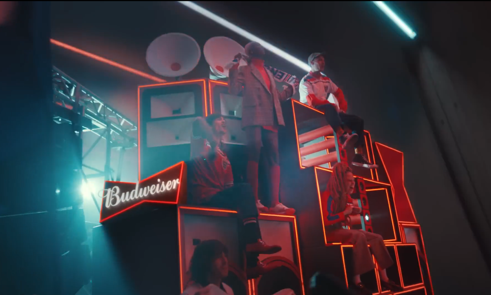 Mensen zitten op een verlichte display met het Budweiser-logo tijdens een evenement.