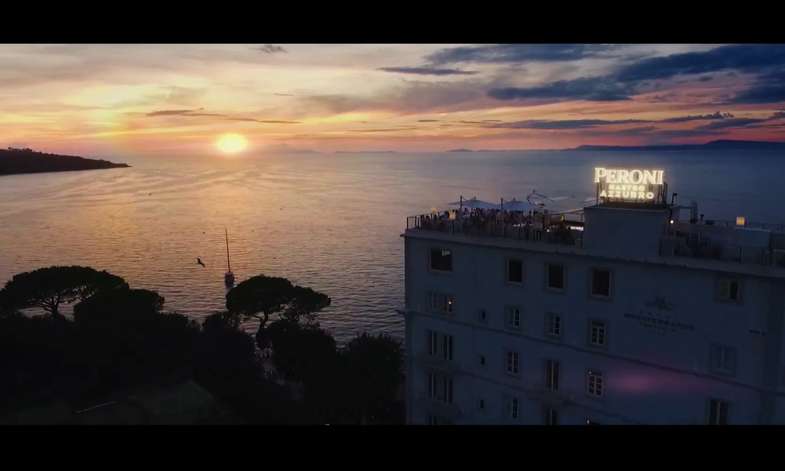 Zonsondergang boven zee met een gebouw en neonreclame voor Peroni.