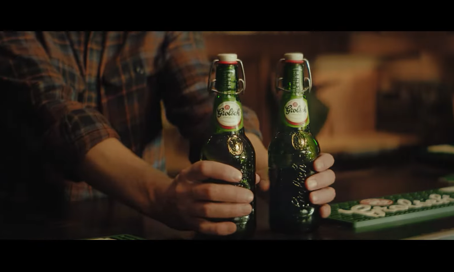 Twee Grolsch bierflessen in handen van persoon met geruite blouse.