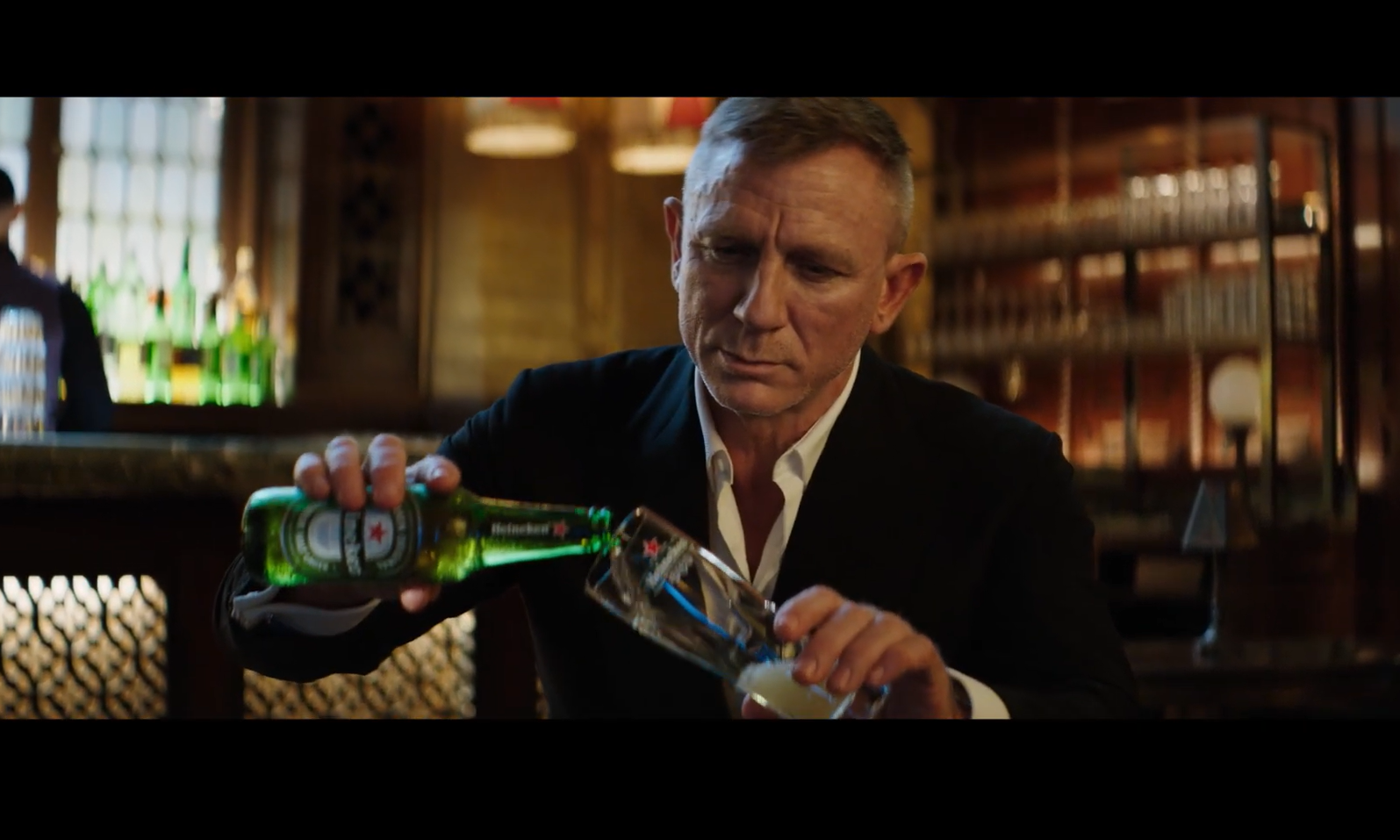 Man in een donker pak giet bier in een glas in een sfeervolle bar.