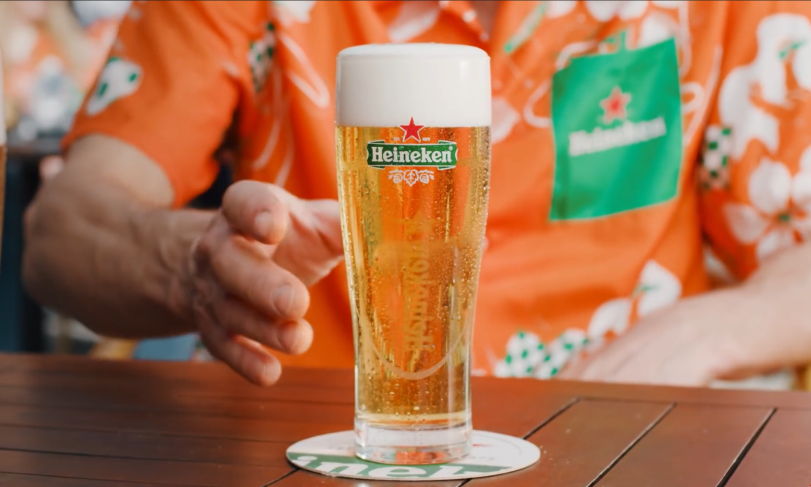 Man reikt naar glas bier op Heineken bierviltje op terras.