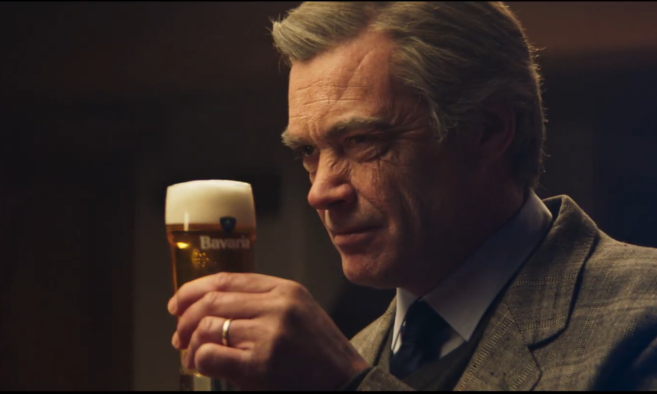 Man houdt een glas Bavaria bier met schuimkraag omhoog in een donkere omgeving.