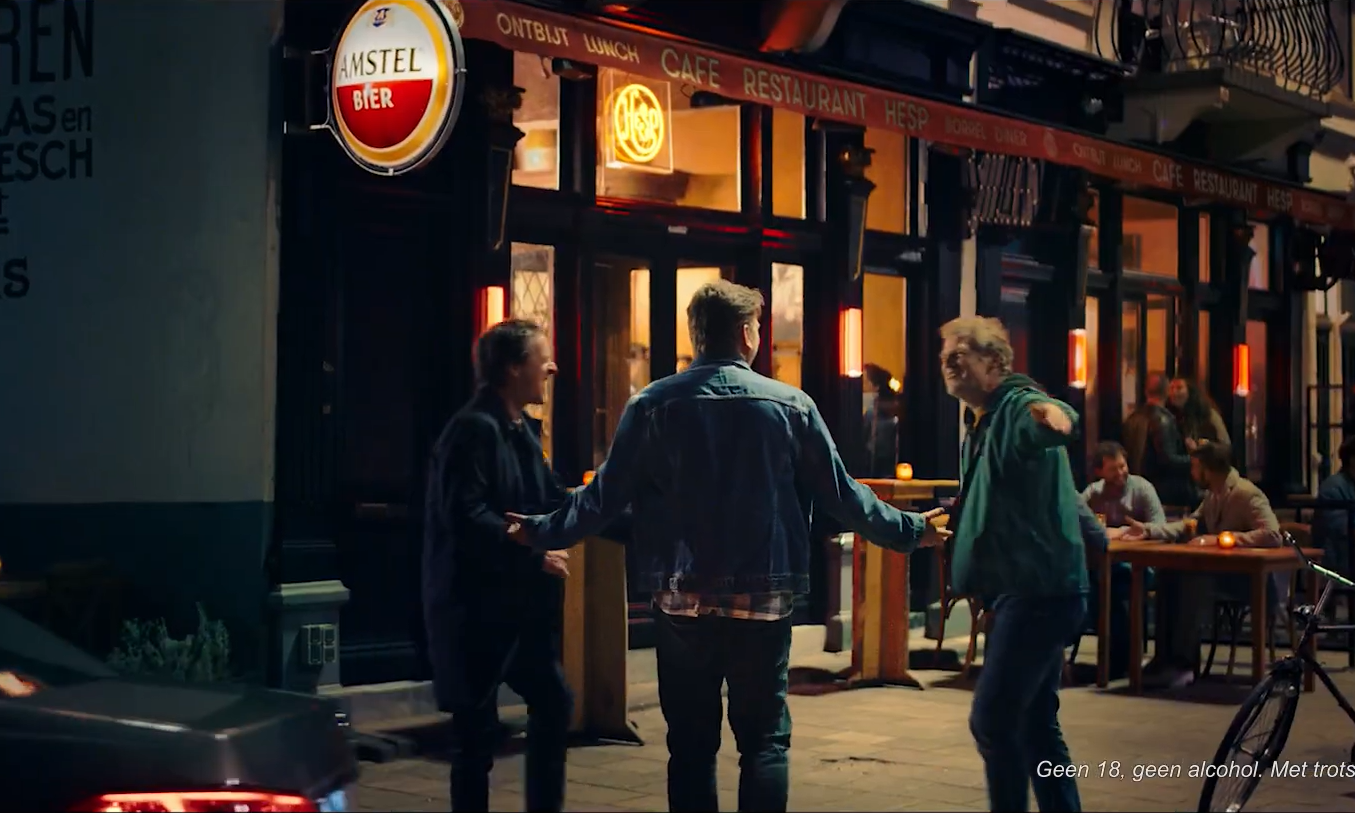Drie vrienden voor een Amstel café in de avond met fiets en mensen op terras.