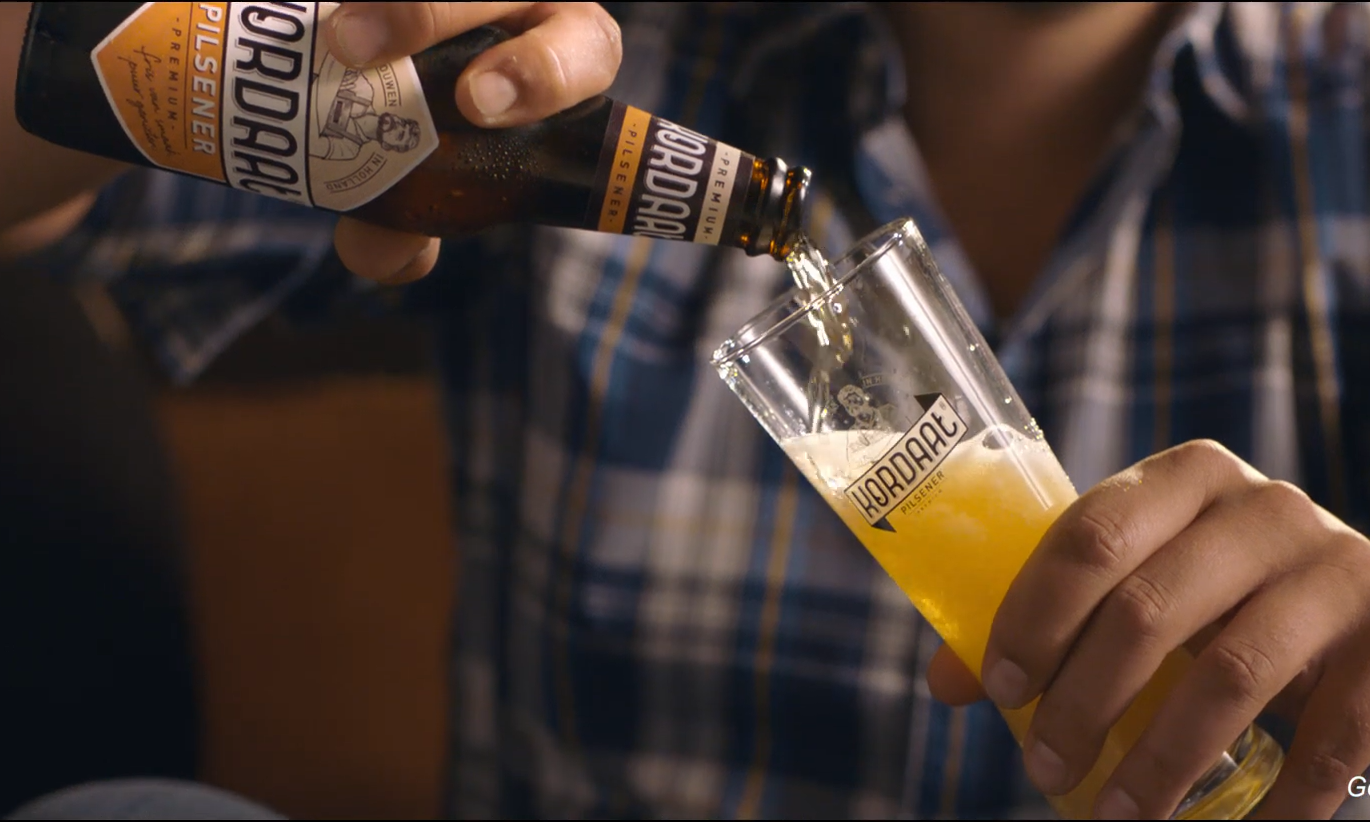 Man schenkt Kordaat pils in een glas in een gezellige setting.