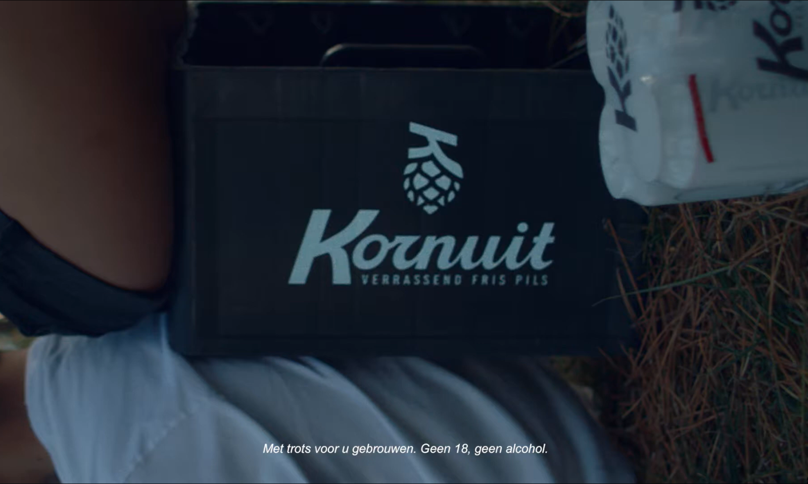 Een man draagt een krat Kornuit pils tegen een groene achtergrond.