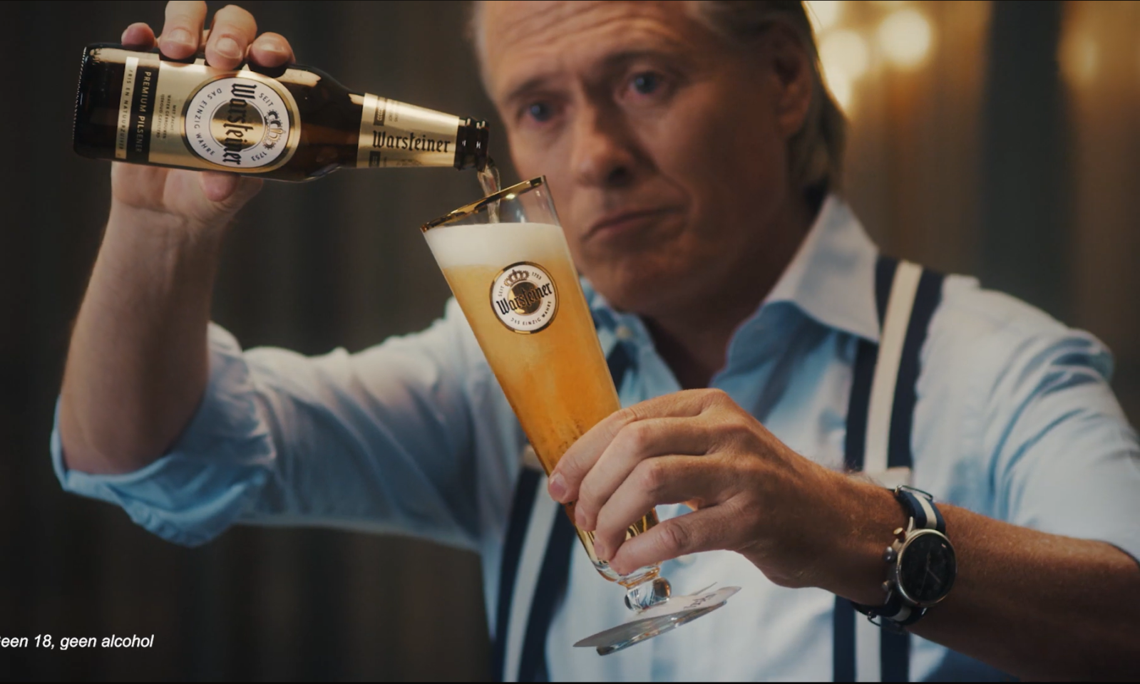 Man schenkt Warsteiner bier in een glas op een donkere achtergrond.