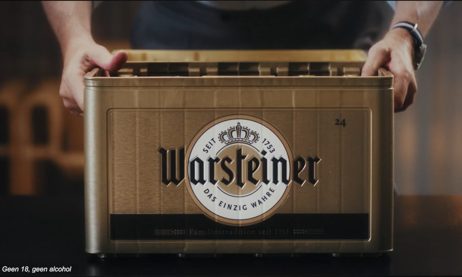 Man tilt een gouden krat Warsteiner bier op een donkere achtergrond.
