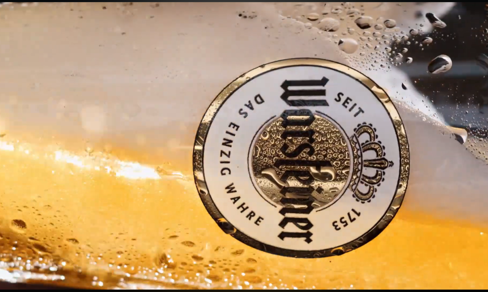 Close-up van een Warsteiner bierfles met het logo en waterdruppels zichtbaar.