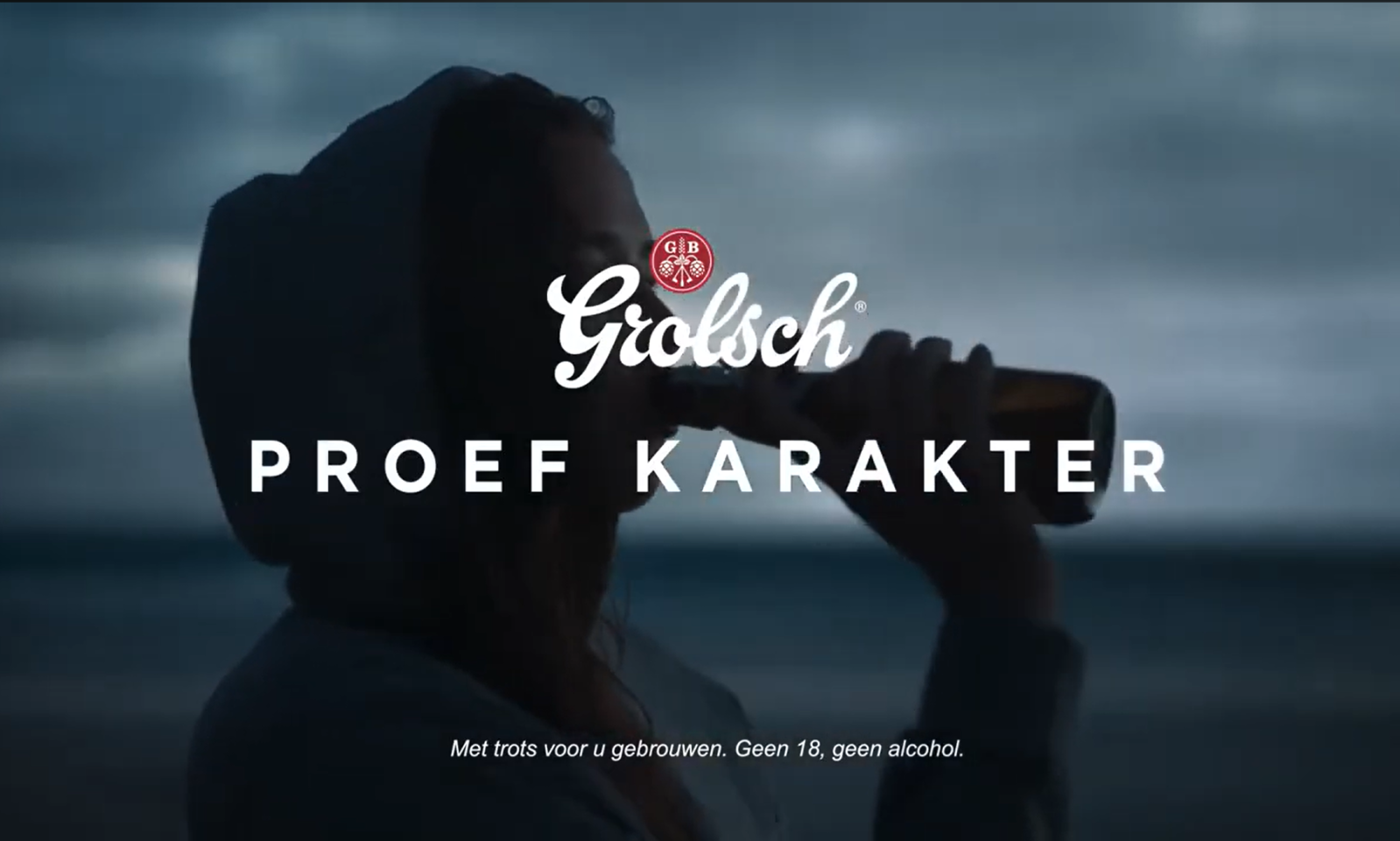 Persoon drinkt Grolsch bier uit fles in schemerige omgeving.