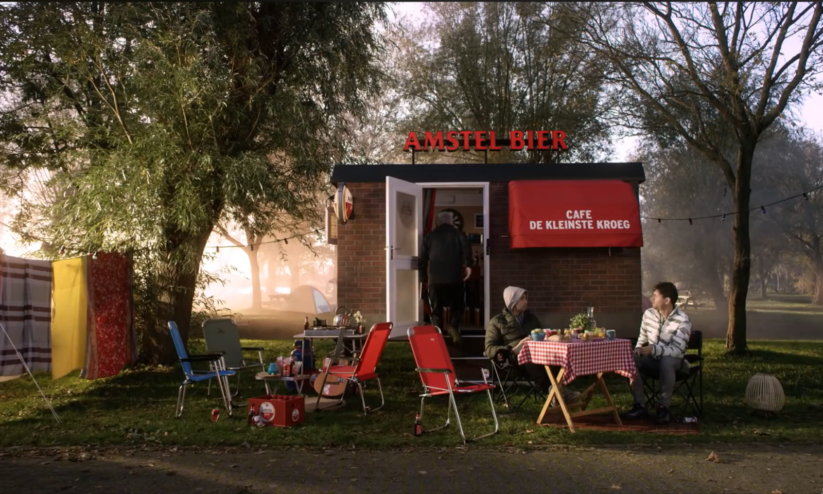 Kampterrein met Amstel Bier-kiosk en mensen buiten in de ochtendzon.