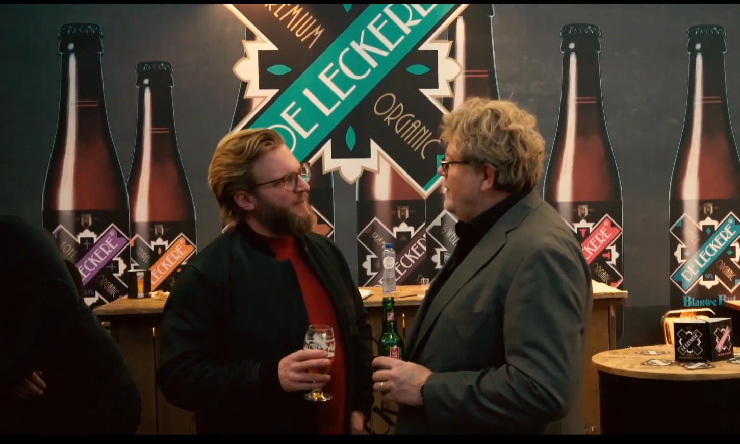 Twee mannen praten met elkaar bij een stand van De Leckere met bier in hun handen.