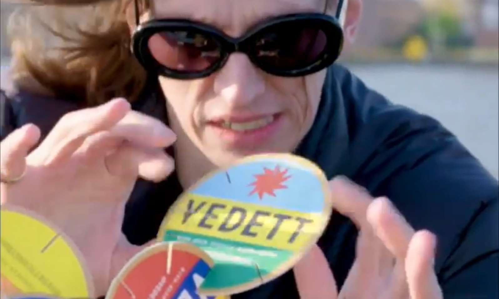 Persoon met zonnebril houdt een bekeronderzetter van Vedett vast.