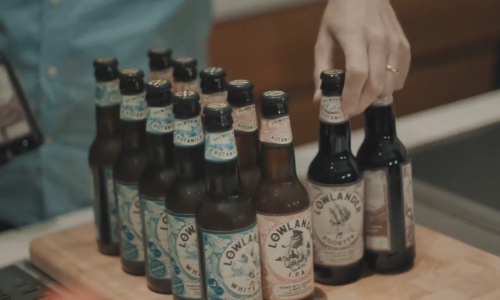 Rij Lowlander-bierflesjes op een houten aanrecht, hand neemt een flesje.