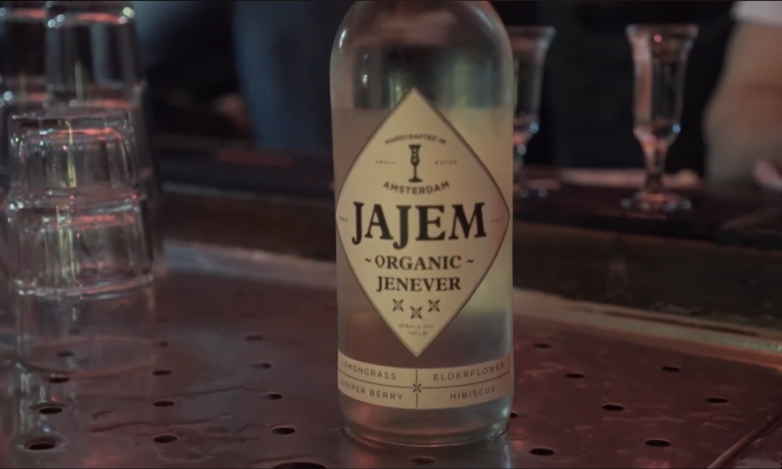 Fles Jajem organic jenever op een bar met glazen op de achtergrond.