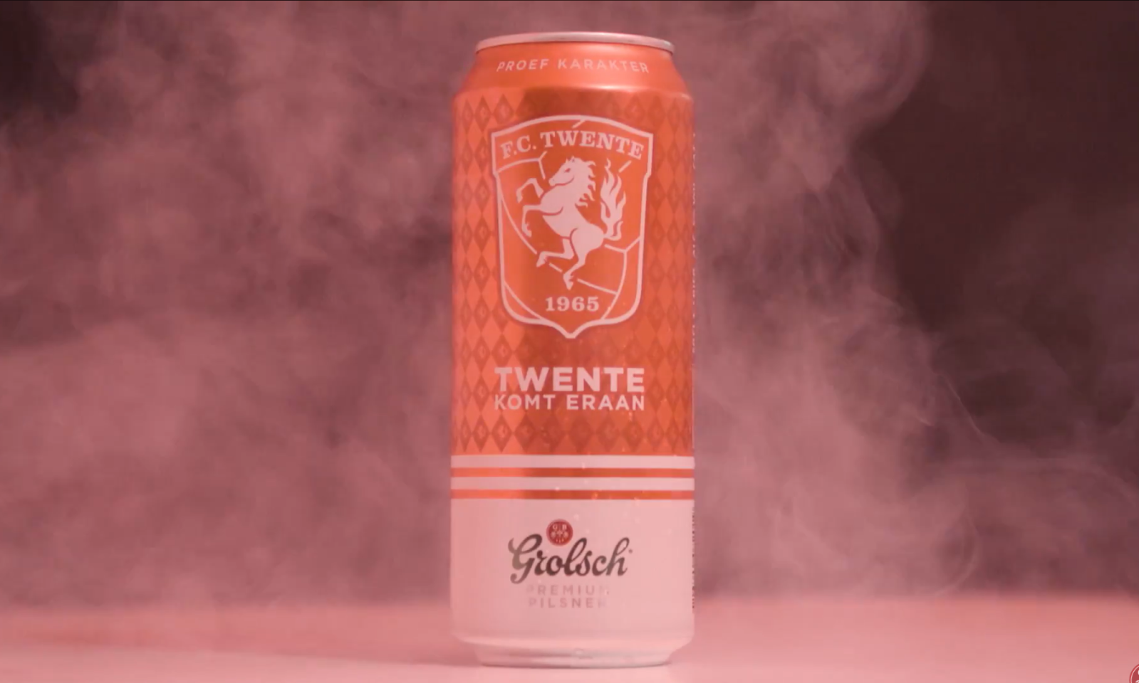Oranje Grolsch bierblik met FC Twente logo in roze rookwolken.