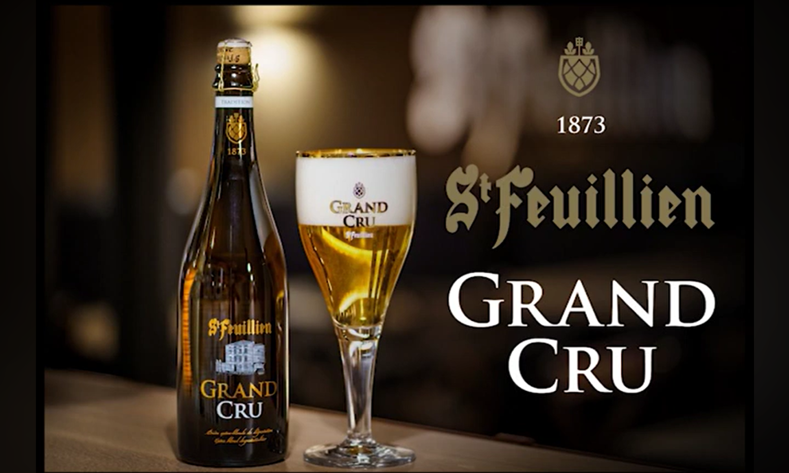 Fles en glas St. Feuillien Grand Cru bier op een tafel met logo en jaartal 1873 op de achtergrond.