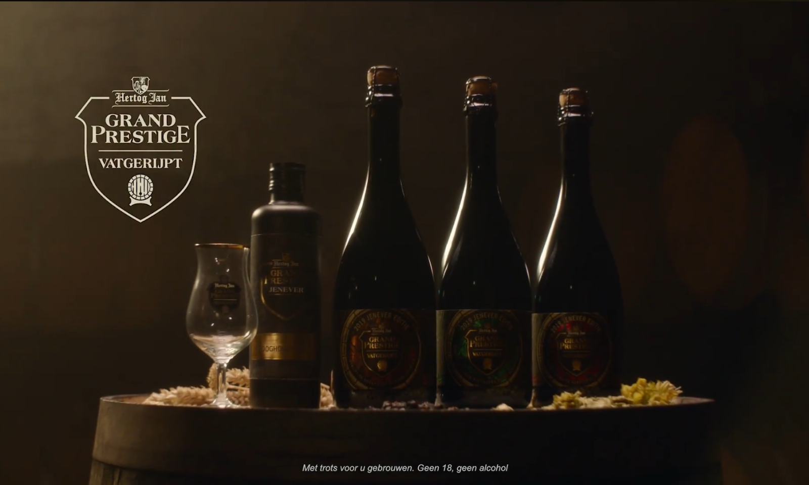 Drie flessen Grand Prestige Vatgerijpt bier en een glas op een houten vat.