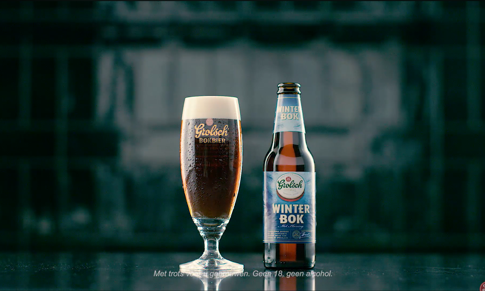 Glas bruinkleurige Grolsch bier naast een fles Grolsch Winterbok op een donkere achtergrond.